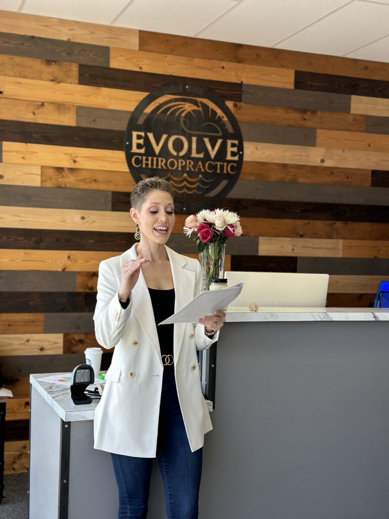 Dr. Stefanie in a white blazer, black top, and jeans holding a paper packet while she explain directions to participants of the vision casting workshop